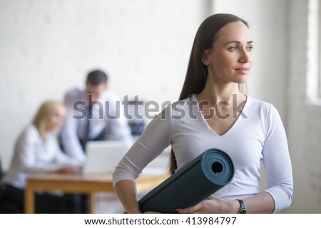 Business and healthy lifestyle concept. Portrait of beautiful sporty young office woman standing with yoga mat at workplace on break time