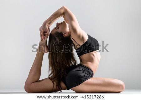 Portrait of beautiful young woman wearing black sportswear working out in studio. Fit sporty girl stretching with closed eyes. Eka Pada Rajakapotasana Pose, One-Legged King Pigeon Posture. Side view