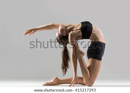 Portrait of beautiful young woman wearing black sportswear working out in studio. Fit sporty girl doing advanced yoga, pilates, fitness. Stretching with closed eyes. Ustrasana, Camel Posture