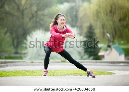 Portrait of sporty woman doing stretching exercises in park before training. Female athlete preparing for jogging outdoors. Runner doing side lunges. Sport active lifestyle concept. Full length