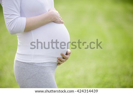 Close-up of torso of young pregnant model standing in park and caressing her belly. Future mom expecting baby. Maternity concept. Copy space for text message