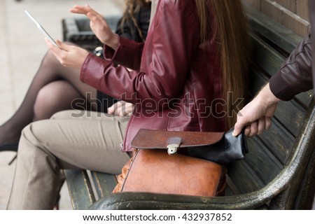 Street thief stealing a wallet from woman bag. Focus on theft hand. Close-up