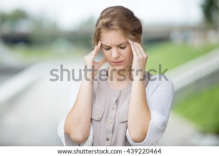 Portrait of stressed beautiful woman walking on the street and holding her head with hands trying to remember something or having headache. Attractive model suffering from pain outdoors in summer