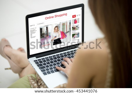 Young shopper woman shopping online on clothing website using laptop. Fashion Caucasian woman model sitting on sofa with notebook, searching for apparel on-line. Close-up. Back view. Focus on screen