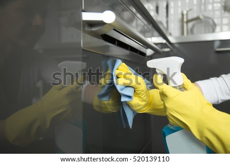 Close up of female hands in rubber protective yellow gloves cleaning the cooker oven panel with rag and spray bottle detergent. Home, housekeeping concept