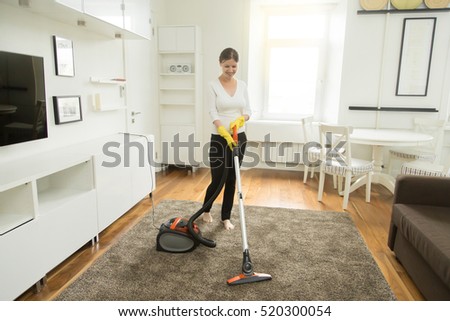 Young smiling woman vacuum cleaning the carpet in the living room, modern scandinavian interior. Busy, cleaning day. Home, housekeeping concept