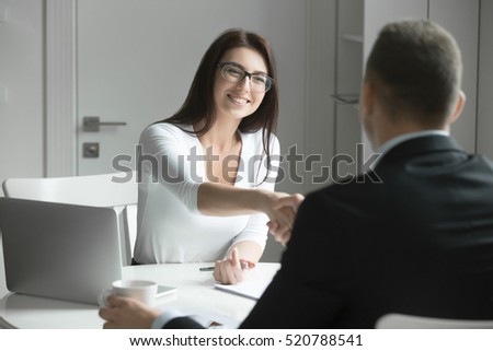 Friendly smiling businessman and businesswoman handshaking over the office desk after pleasant talk and effective negotiation, good relationships. Business concept photo