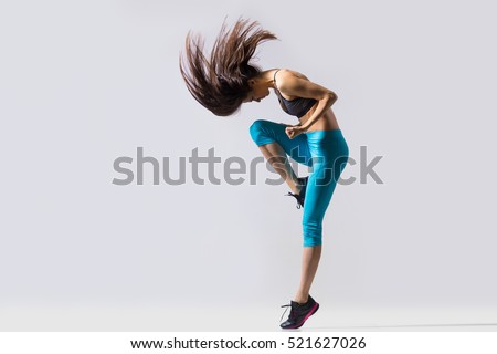 One cool beautiful young fit modern dancer lady in blue sportswear warming up, working out, dancing with her long hair flying, full length, studio image on gray background