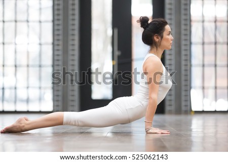 Full length side view portrait of beautiful young woman working out in luxury fitness center, doing yoga or pilates exercise without mat on wooden floor. Upward facing dog, Urdhva mukha svanasana
