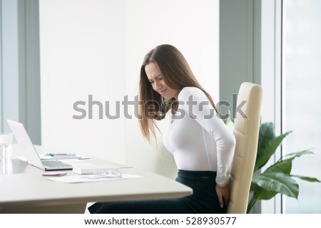 Profile portrait of an irritated young businesswoman woman at the office, feeling her back tired after working at laptop, uncomfortable chair, feeling severe back ache, itching, difficulty sitting