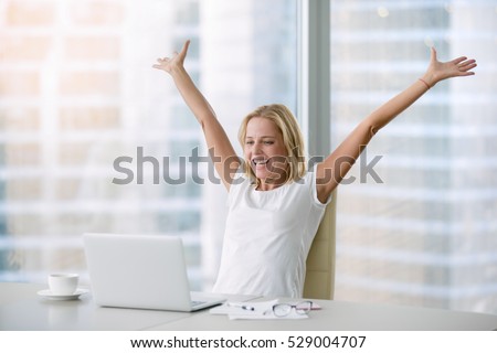 Young attractive woman at a modern office desk, with laptop, stretching her arms with extreme joy special prize winner, office holiday party, found a job, got a date invitation, end of the working day