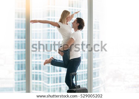 Young happy traveller couple laughing, embracing, having fun, feeling euphoria, family moved into a bigger flat, inherit a property, rented cool apartment on trip wedding gift, travelling in honeymoon
