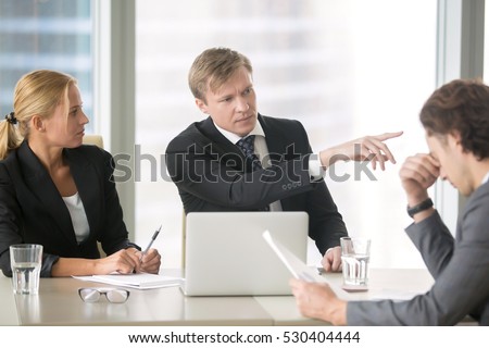 Furious boss scolding young frustrated intern, dismissing him with hand gesture. Ineffective stressed office worker receiving dismiss notification sitting at table, listen to irritated boss yelling