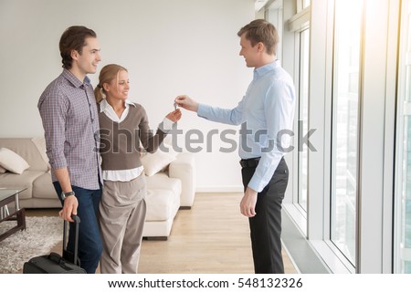 Young attractive married couple in love buying or renting new apartment, meeting with real estate agent, occupiers moving into rented accommodation, starting family life, moving out from another city
