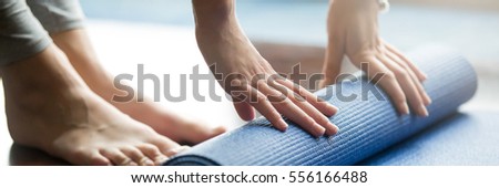 Close-up of woman folding blue yoga or fitness mat after working out at home in living room. Healthy life, keep fit concepts. Horizontal shot. Horizontal photo banner for website header design
