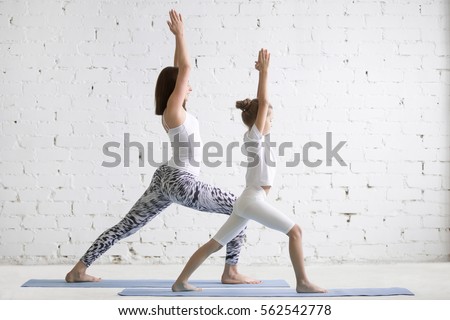 Kids yoga female teacher training girl child, practicing yoga, standing in Warrior one exercise, Virabhadrasana I pose, working out wearing sportswear, indoor full length, white loft studio background