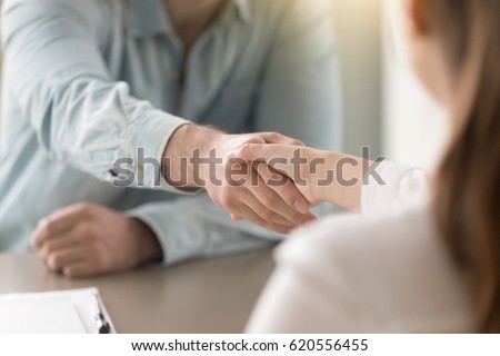 Businessman shaking female hand above the table. Business agreement and partnership concept. Partners closing a deal, view over the shoulder. Formal greeting  gesture, effective negotiations