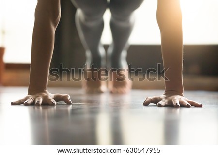 Young woman practicing yoga, doing Push ups or press ups exercise, phalankasana Plank pose, working out, wearing sportswear, grey pants, indoor, home interior, living room floor. Close-up of hands