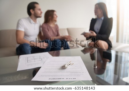 Young renters couple sitting on couch discussing renting apartment with real estate agent, focus on rental agreement and keys, property lease contract. Looking for accommodation, long-term tenancy