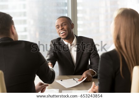 Excited smiling black businessman handshaking white partner at meeting, successful african applicant getting hired, got a job, satisfied multiracial businessmen shaking hands after signing document