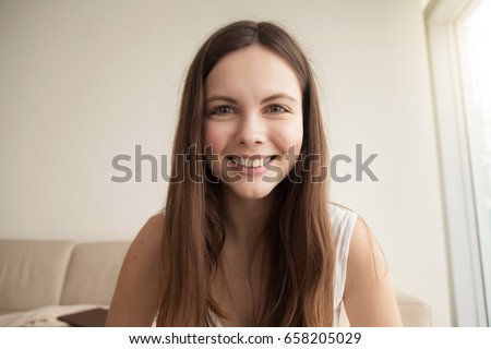 Headshot portrait of smiling young woman. Teen girl with happy facial expression looking at camera with joy, communicating with friends via internet telephony, making skype call. Close up. Front view