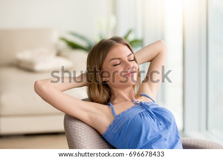 Woman relaxed sitting in chair with closed eyes, hands behind head resting at home, feeling positive, dreaming about future. Attractive lady enjoying weekend, satisfied with life. Breathing fresh air