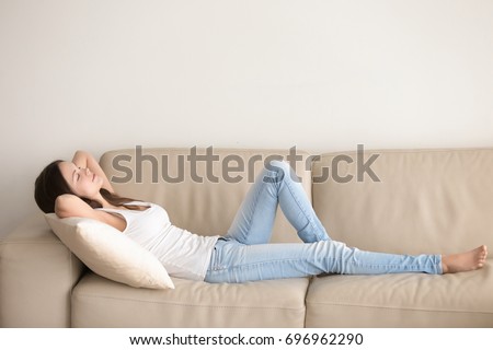 Young woman lying on couch cushion with eyes closed, relaxing on cozy sofa pillow, relaxed girl taking nap at home hands behind head, breathing fresh air, no stress, enjoying day off in living room