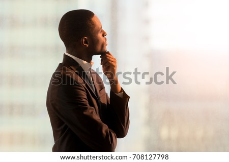 Portrait of pensive african american businessman standing near window and thinking about decision, dreaming of success, pondering new startup. Handsome black business leader imagining company future