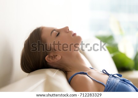 Calm teen girl relaxing on sofa at home, breathing fresh air with eyes closed leaning on comfortable couch, young woman meditating in cozy living room, practicing yoga, no stress, side view head shot