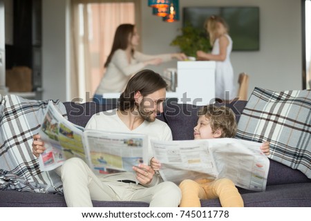 Happy dad and son reading newspapers together on couch, father with little boy looking at each other holding paper news, funny kid copying imitating daddy sitting at home on sofa, intelligent child