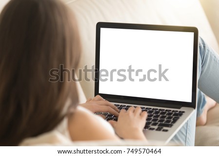Woman on sofa working on laptop with mockup blank screen. Empty copyspace on monitor for  advertisement, language learning ad, online shopping website, social media site. Close up, focus on screen.