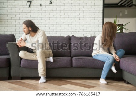 Unhappy sad couple sitting apart on couch in living room after quarrel, frustrated man and woman turning their back ignoring having conflict at home, can not find compromise, misunderstanding concept