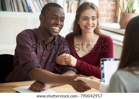 Smiling multiracial couple customers shaking hands with mortgage broker or financial advisor, happy attractive black and white family handshaking lawyer bank worker taking loan, making purchase deal