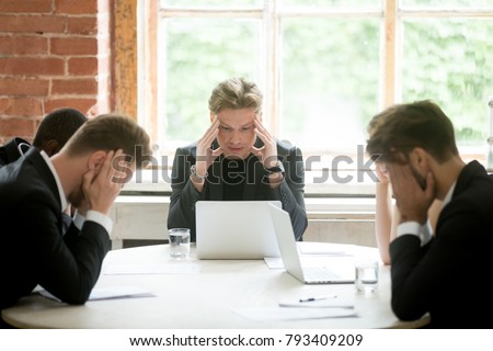 Stressed boss and executive team searching problem solution at meeting, partners holding heads in hands depressed by failure bad news, feeling desperate about company bankruptcy or financial crisis