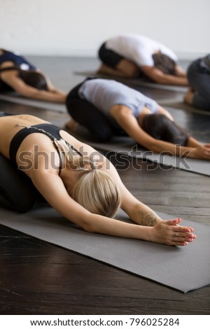 Group of young sporty people practicing yoga lesson with instructor, stretching in Child exercise on mat, Balasana pose, working out, indoor close up, students training in club, studio