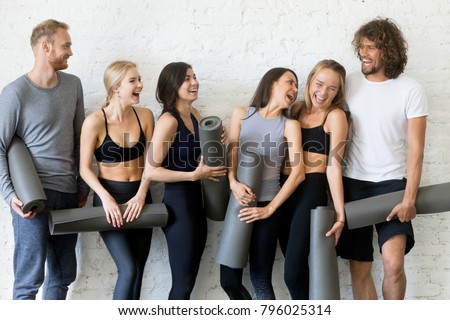 Group of laughing young sporty people standing at white wall. Having rest after practices, inviting, social atmosphere in yoga club, portrait of smiling students spending good time, indoor loft studio