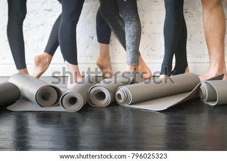 Yoga mats in a roll. Rubber carpets for individual hygiene, soft surface to perform fitness exercises, essential piece of sport gear from nonslip material. Club floor and legs at background. Close up