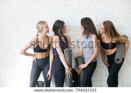 Group of young sporty girls with fitness mats talking. Chatting while having a break, exchanging news, sharing diet and exercise tips, making true friends in yoga community, studio