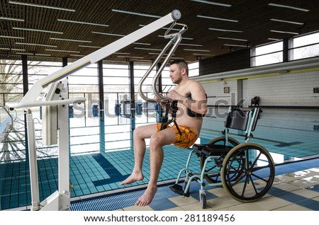 Disabled man in a swimming pool. Lift for the descent of people with disabilities into the pool. Wheelchair.