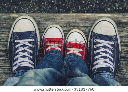 Children's legs and feet in shoes adult sneakers with each other.
