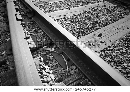 A black and white photo of train tracks isolated with gravel spreading across the railway.