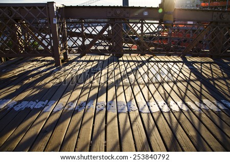 A photograph of shadows and lines crossing the wooden path of the Brooklyn Bridge in New York City.