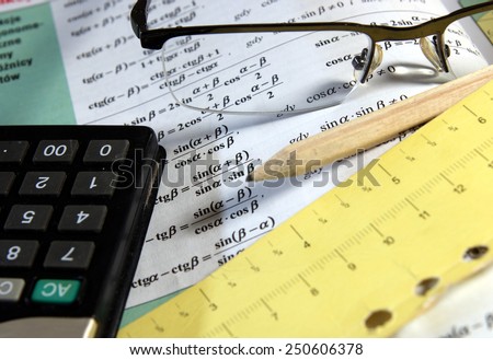 Math study for the exam set (book, pencil, glasses, calc) - Background shows trigonometry formulas which have focus on only small part of the image to underline the subject - rest is blur by intention