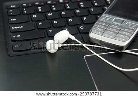 Telemarketing and remote work set: Laptop (notebook), headphones and cell phone on the keyboard. Focus intentionally on only a small part of the image (to underline the subject)