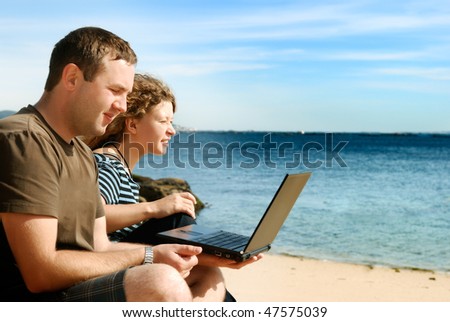 man and woman working with computer at beach