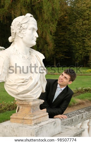 Young man in dark suit in park with old (XIX cent.) sculpture