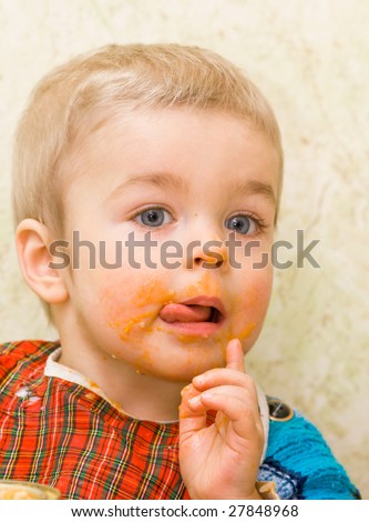 Cute little boy licking his lips during a meal, stained with squash