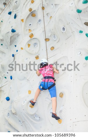A female teenager climbing a rock wall halfway to the top