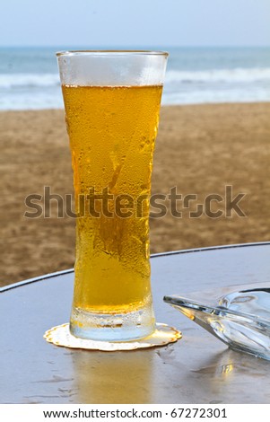 Cold and refreshing,  tall glass of beer giving off a golden glow set against an ocean view