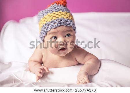 little girl lying on her stomach on the bed,big  blue eyes, and fun to knit cap on his head, baby